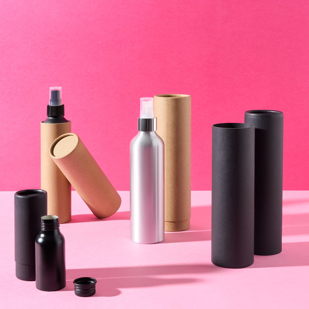 Collection of aluminium bottles with telescopic tubes and pump or spray caps on a pink background. 